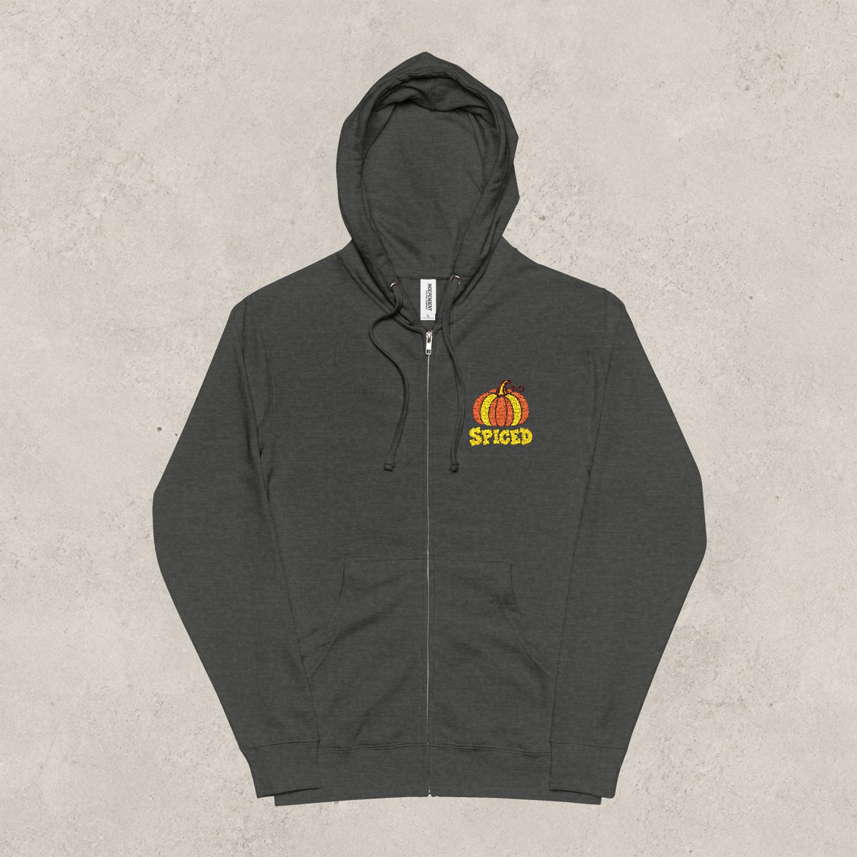 A dark charcoal gray zip-up hoodie with a small orange and yellow pumpkin graphic and the word 'SPICED' on the left chest, displayed against a textured light gray background.