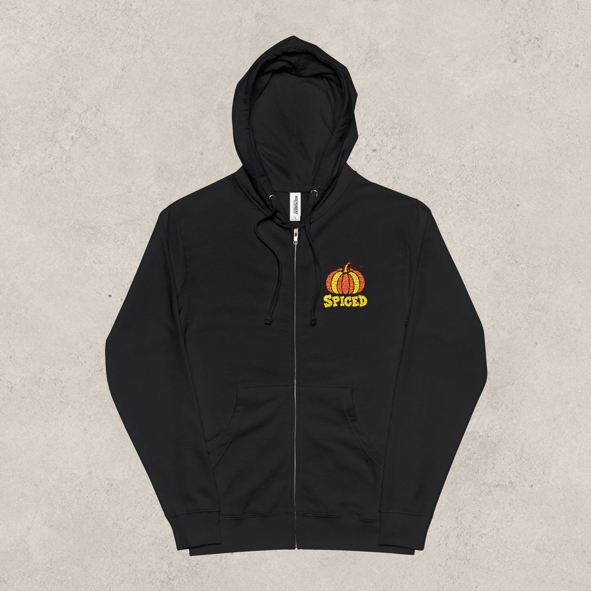 A black zip-up hoodie with a small orange and yellow pumpkin graphic and the word 'SPICED' on the left chest, displayed flat against a textured light gray background.