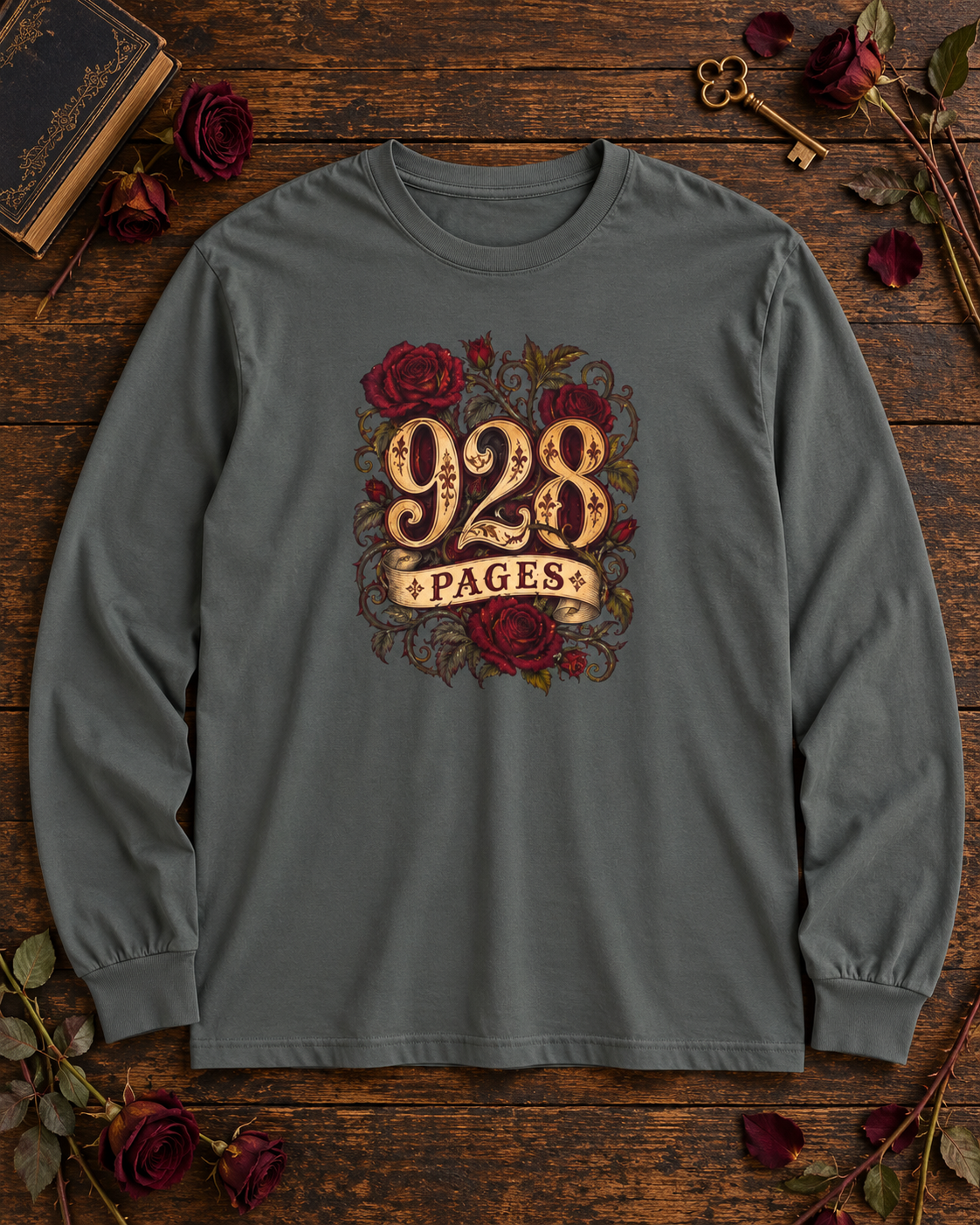 Pepper gray long sleeve shirt with ornate gold 928 PAGES lettering wrapped in red roses and thorny vines, on a wood table with an antique book and dried roses